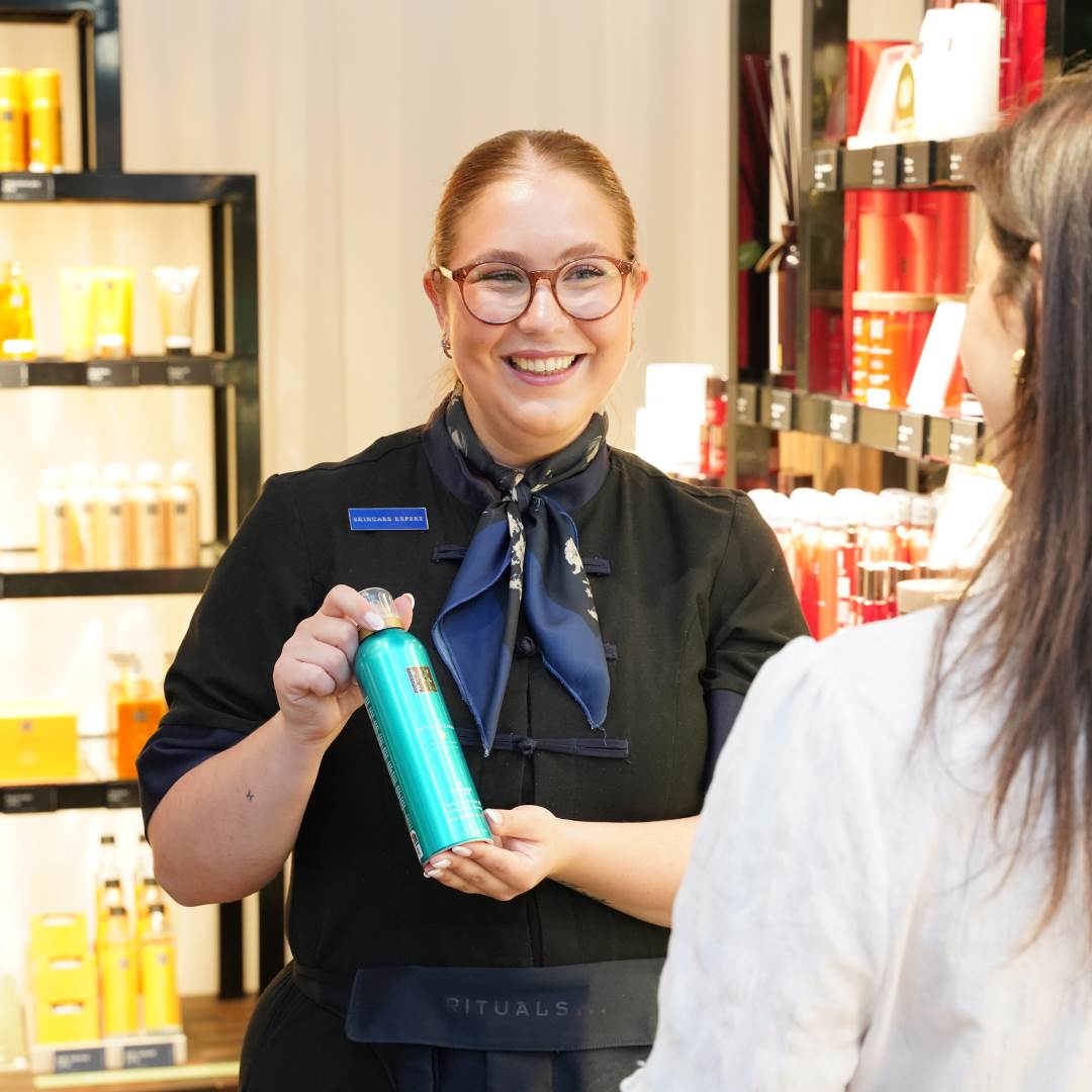 Smilende medarbejder fra Rituals i Randers viser kunde showerfoam.